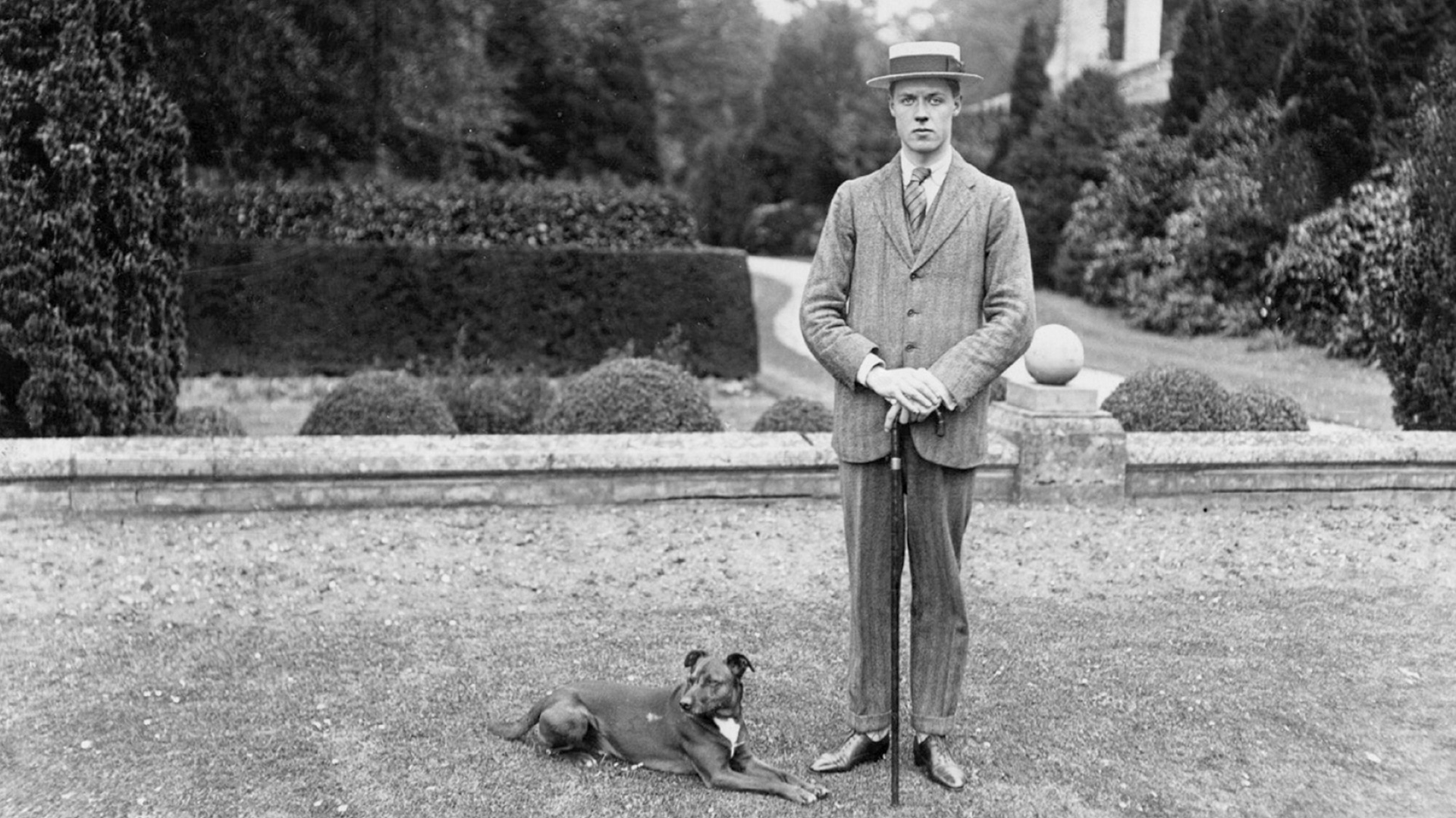 Dapper early 20th century man with hat and dog holding a cane