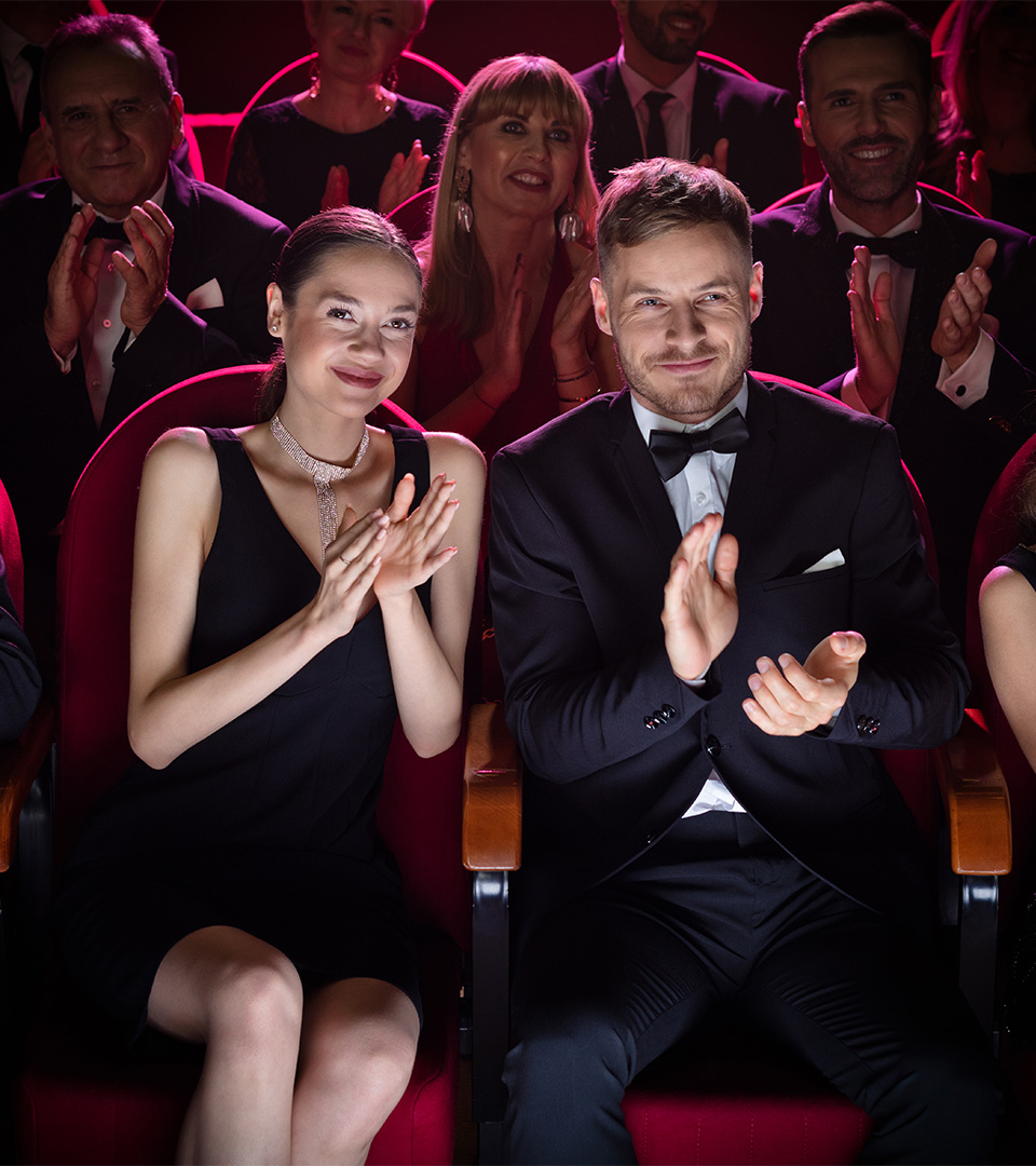 aria mature couple clapping while watching theatrical performance. Happy man and woman are enjoying movie during weekend. They are sitting amidst crowd.