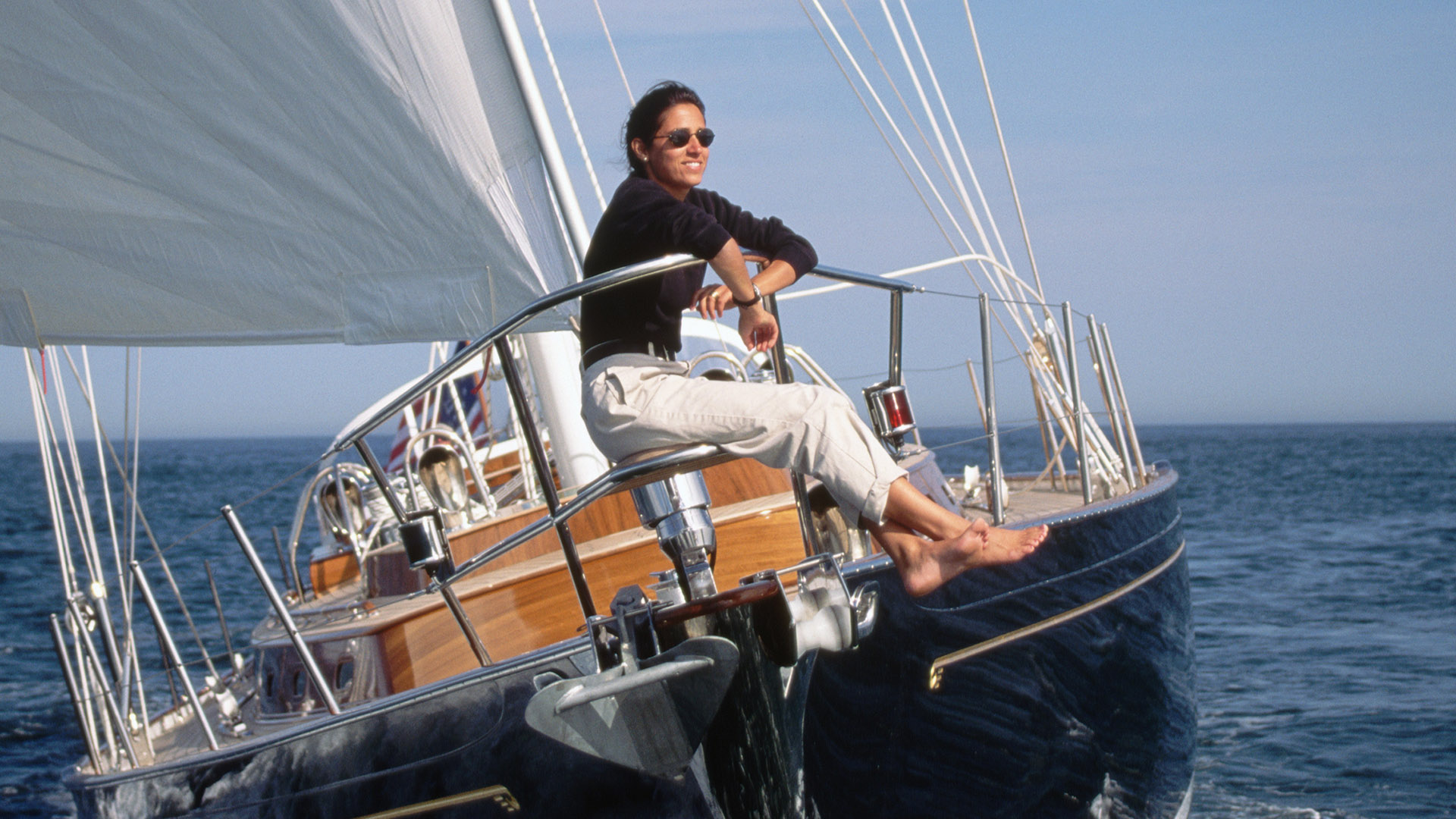 A woman rides on the bow of a sailboat as it cruises full sail