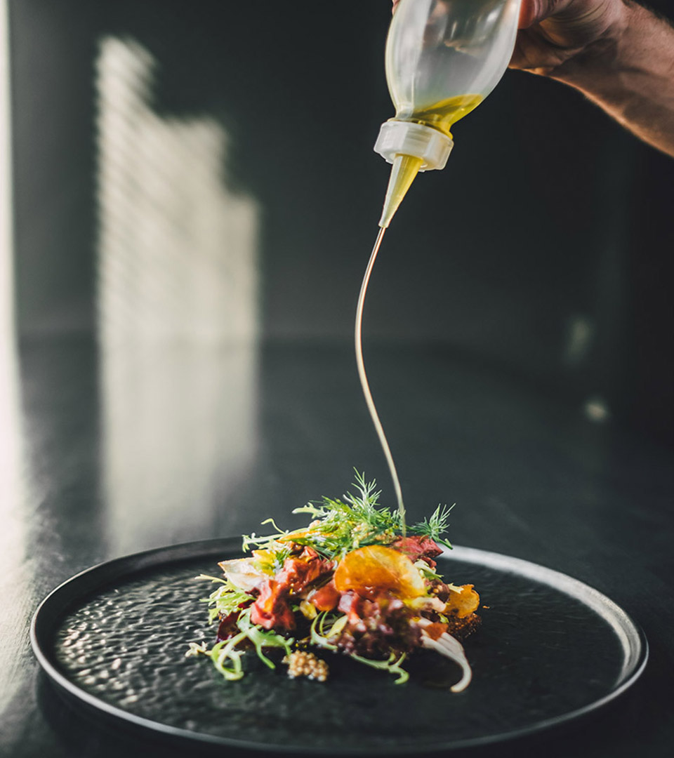 vela seaport hand pouring olive oil on a small salad